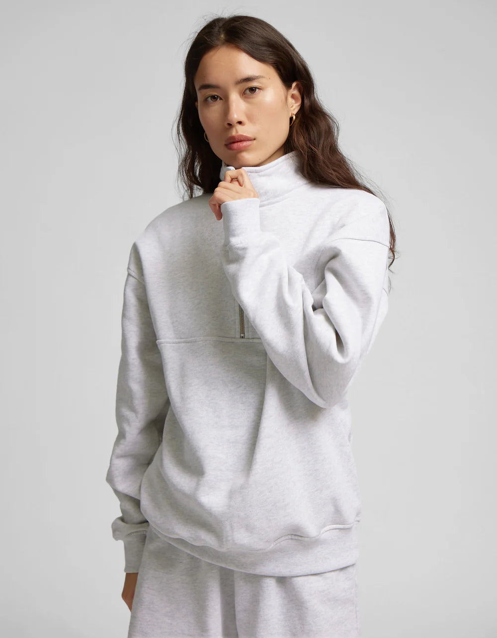 A person is wearing the Organic Quarter Zip from Colorful Standard, a light gray organic cotton pullover with a high collar, standing against a neutral background.