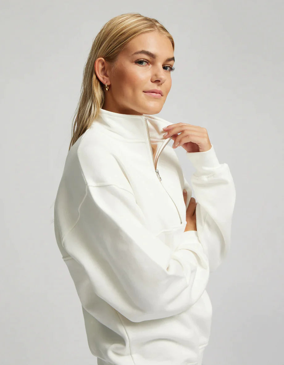 A woman wearing a white Colorful Standard Organic Quarter Zip and sweatpants made of organic cotton.