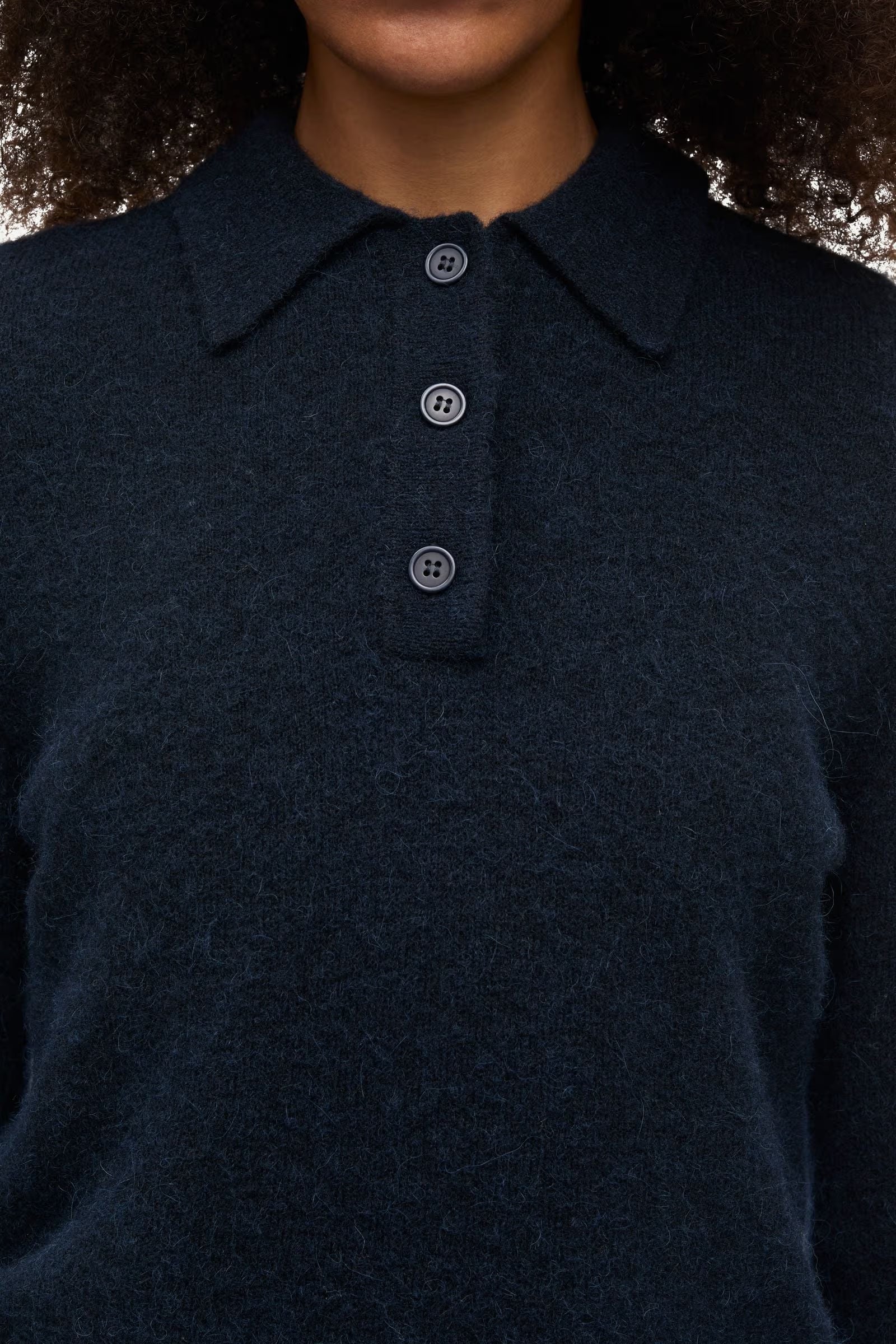 Close-up of a person wearing the Sanoura LS Polo in navy by Samsøe Samsøe— a luxurious long-sleeve sweater crafted from a wool alpaca blend, featuring a fuzzy texture, polo collar, and four black buttons on the placket.