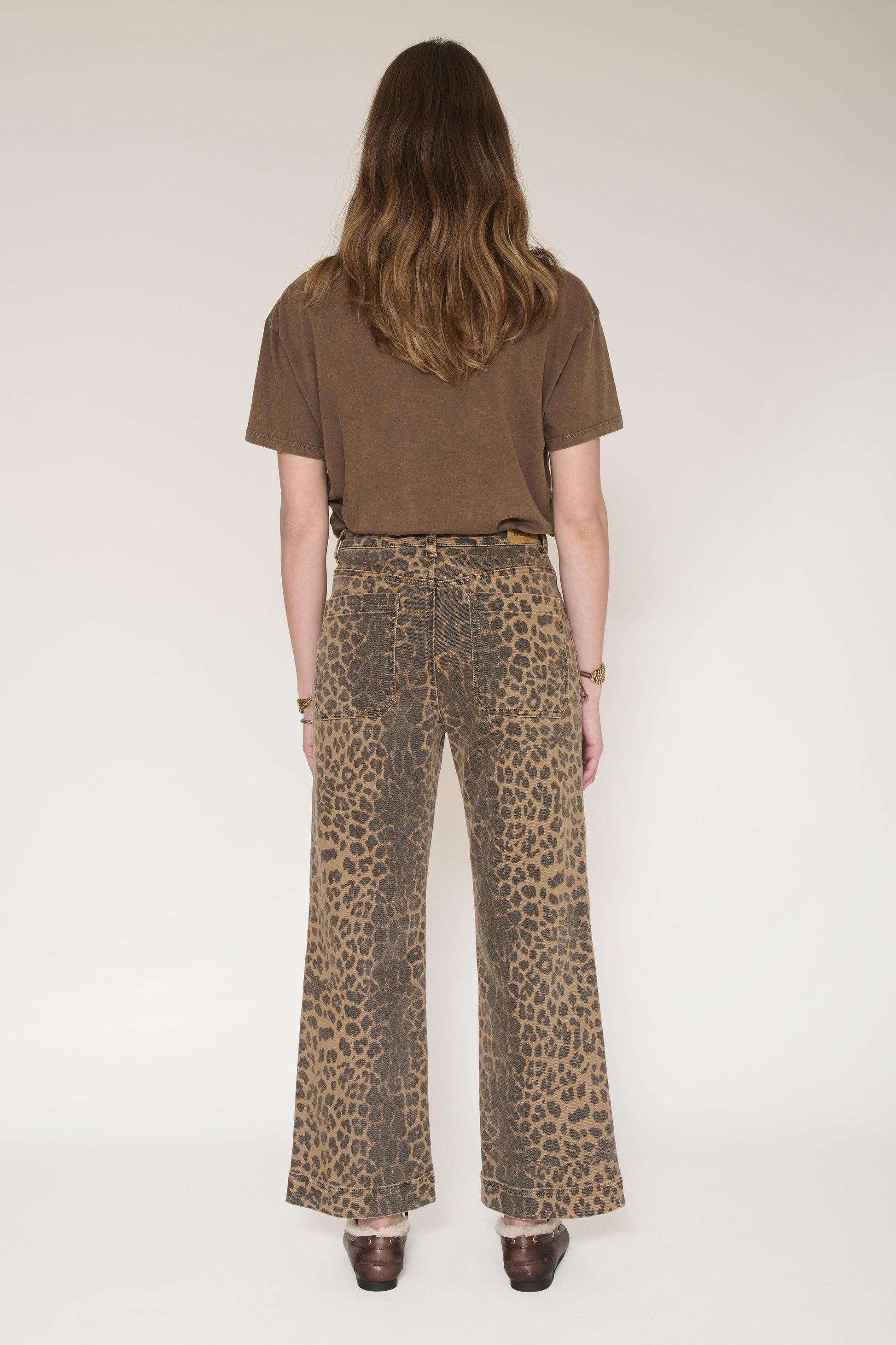 A model shown from the back wearing high-waisted leopard-print wide-leg pants and a brown short-sleeve t-shirt, standing against a plain light background.