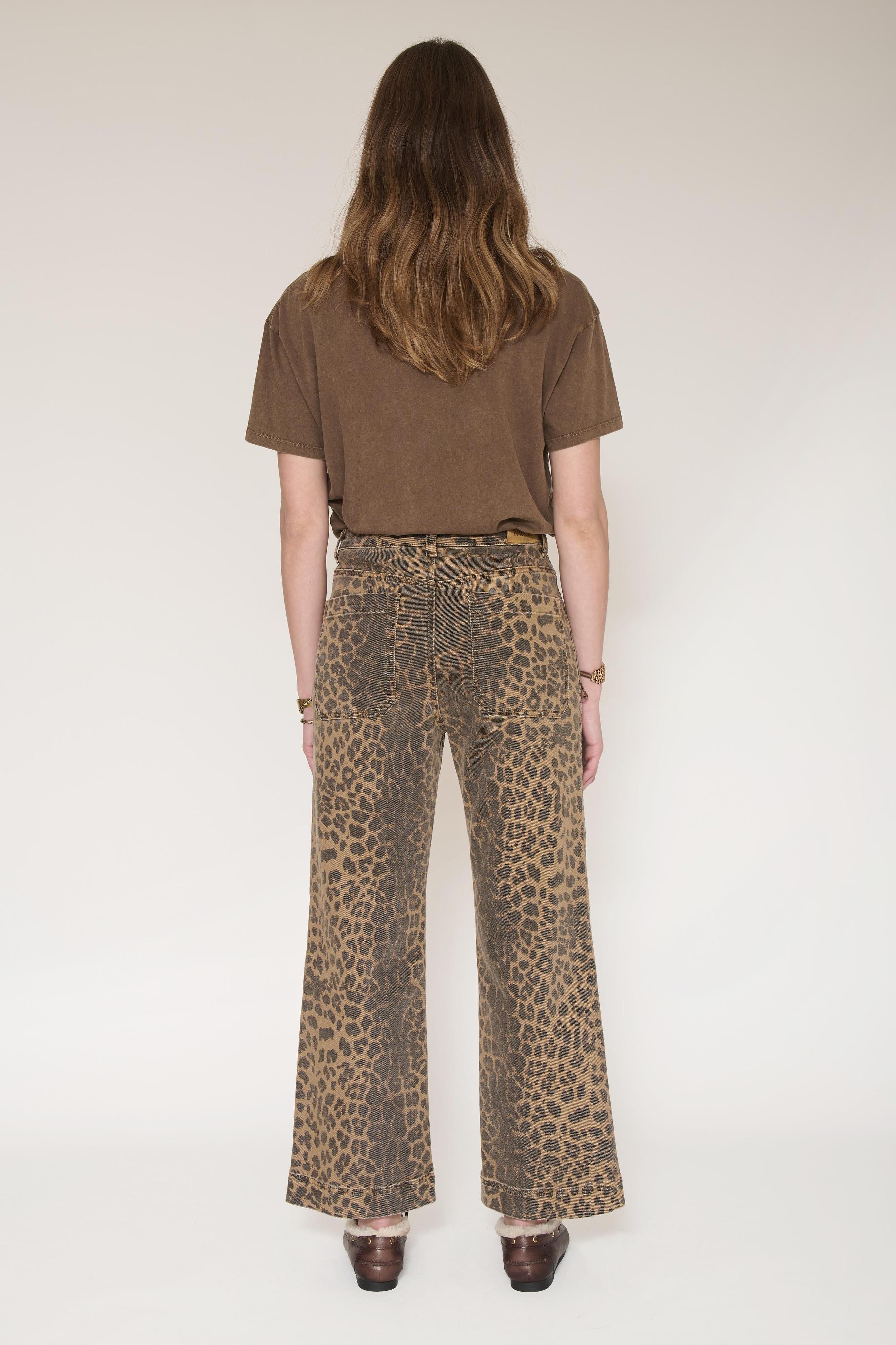 A model shown from the back wearing high-waisted leopard-print wide-leg pants and a brown short-sleeve t-shirt, standing against a plain light background.