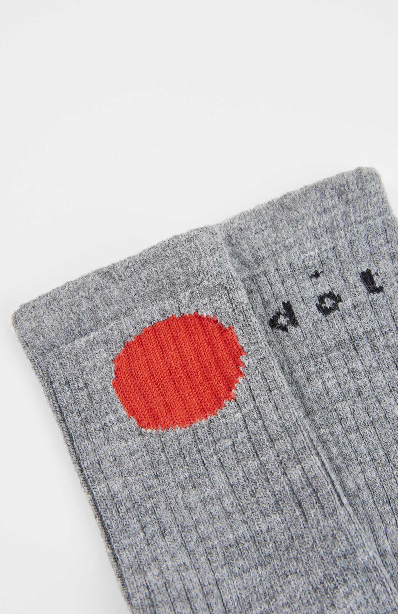 The Bioti Mid-Calf Socks by Loreak Mendian are grey, ribbed, and feature a large red circle near the top plus partial black text on one sock.