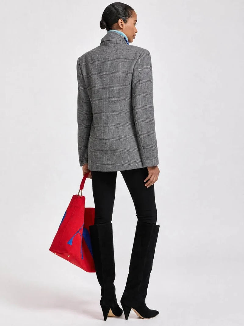A model shown from the back wearing a gray plaid blazer, black skinny pants, and black over-the-knee boots, holding a red tote bag with blue accents against a plain white studio background.