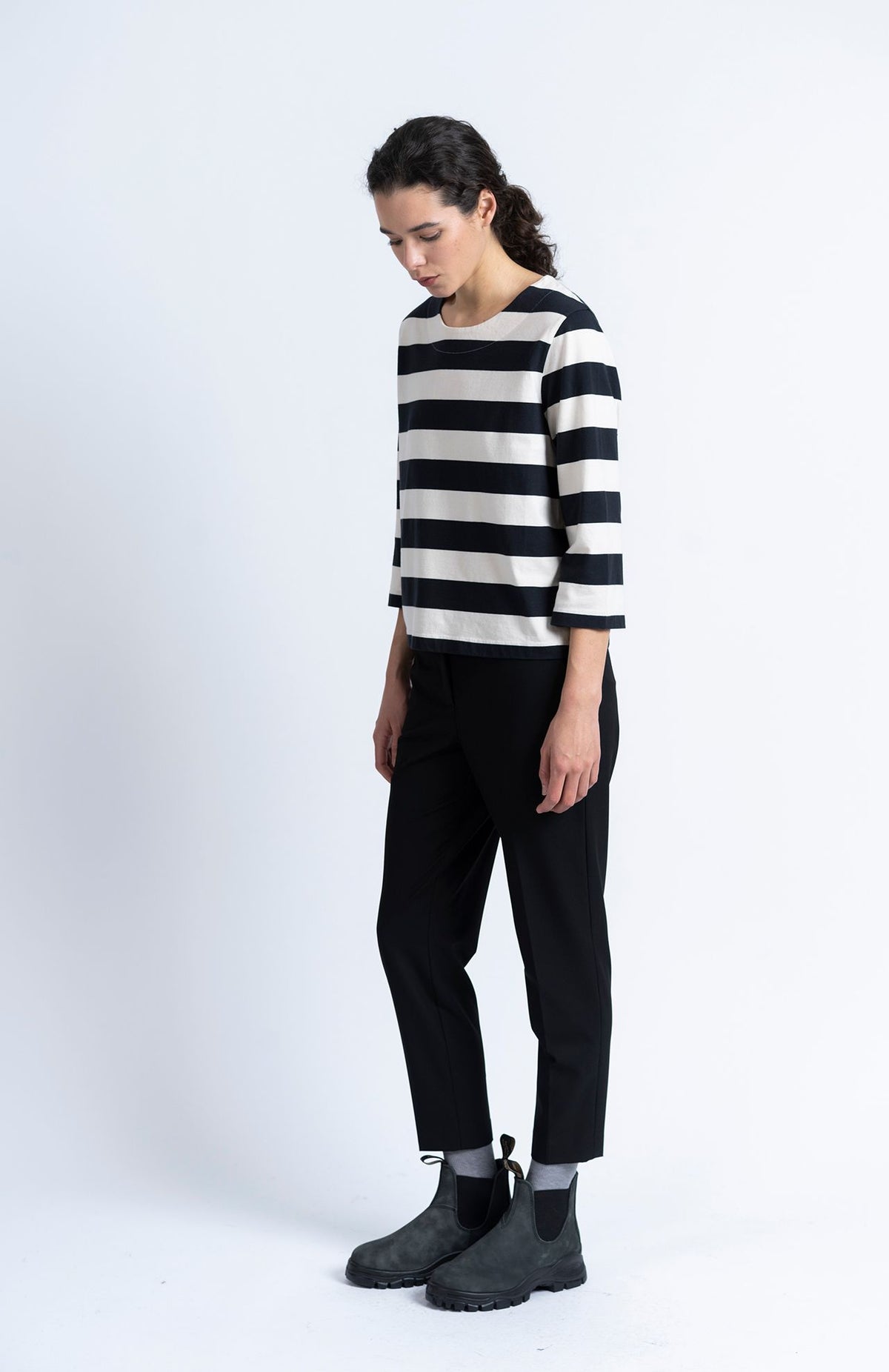 A person wearing a black and white horizontal striped top, Loreak Mendian Alaiak Trouser - Black joggers, and black ankle boots.