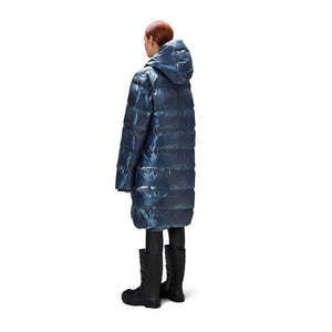 person wears long metallic blue padded puffer by Rains which has a double zip detaile and hood. 