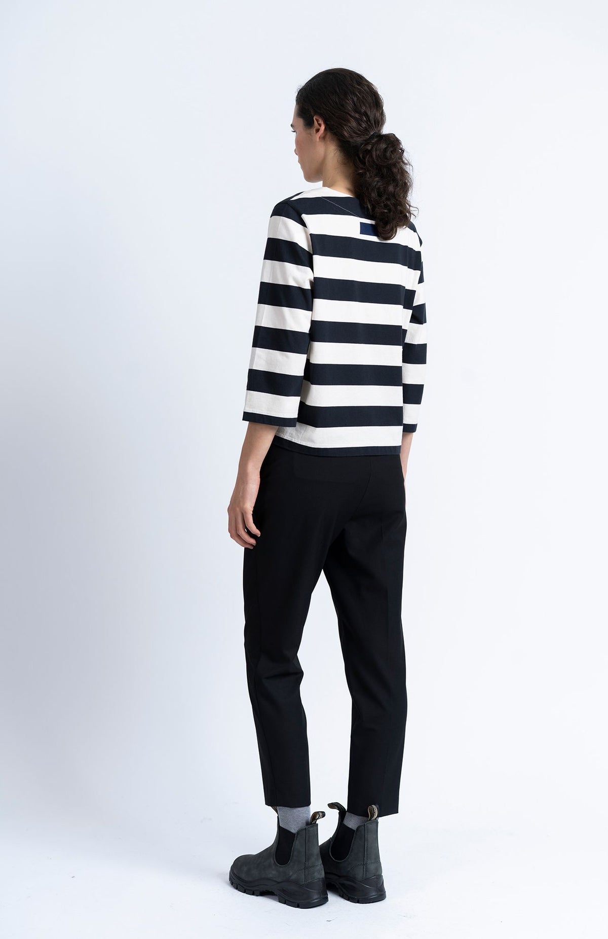 A person seen from the back wearing a striped long-sleeved shirt, Alaiak Trouser - Black joggers, and black ankle boots.