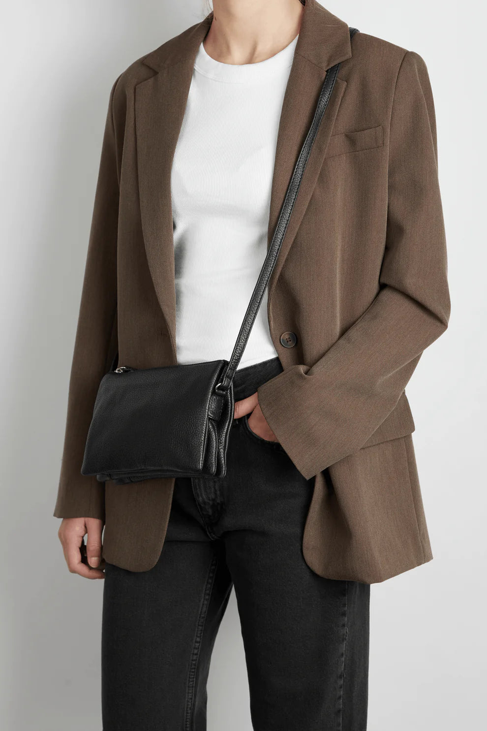Person wearing a brown blazer and black jeans with a white t-shirt, carrying a Markberg Grain Crossbody Bag.