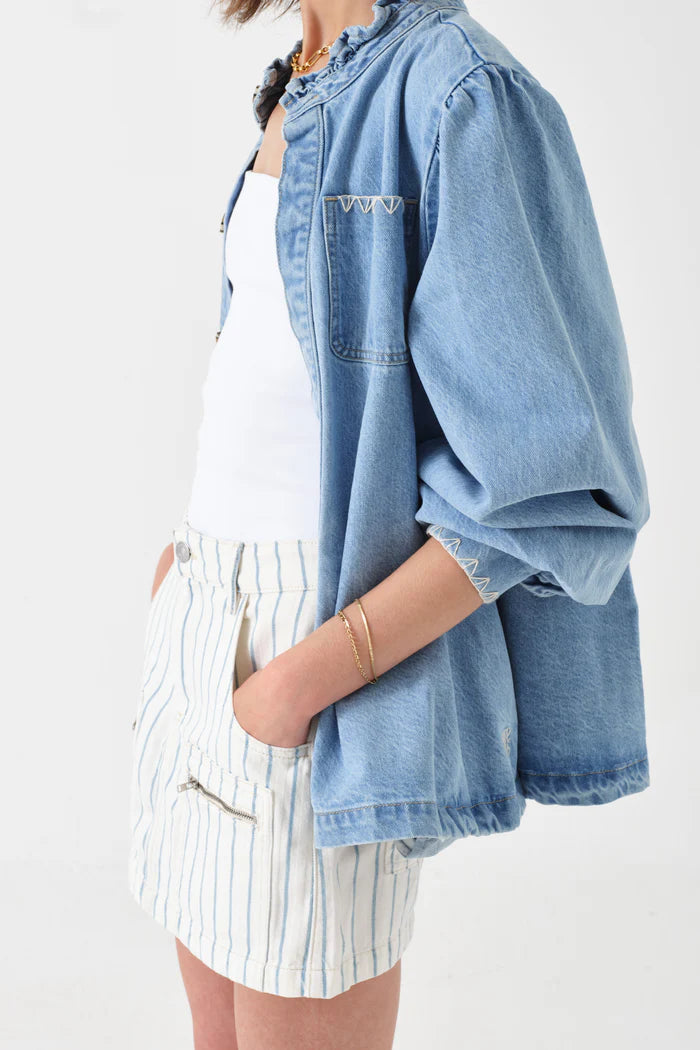 Someone wearing the Seventy & Mochi Dana Denim Jacket in Sunbleached over a white top and white shorts with blue vertical stripes, with one hand in the pocket.