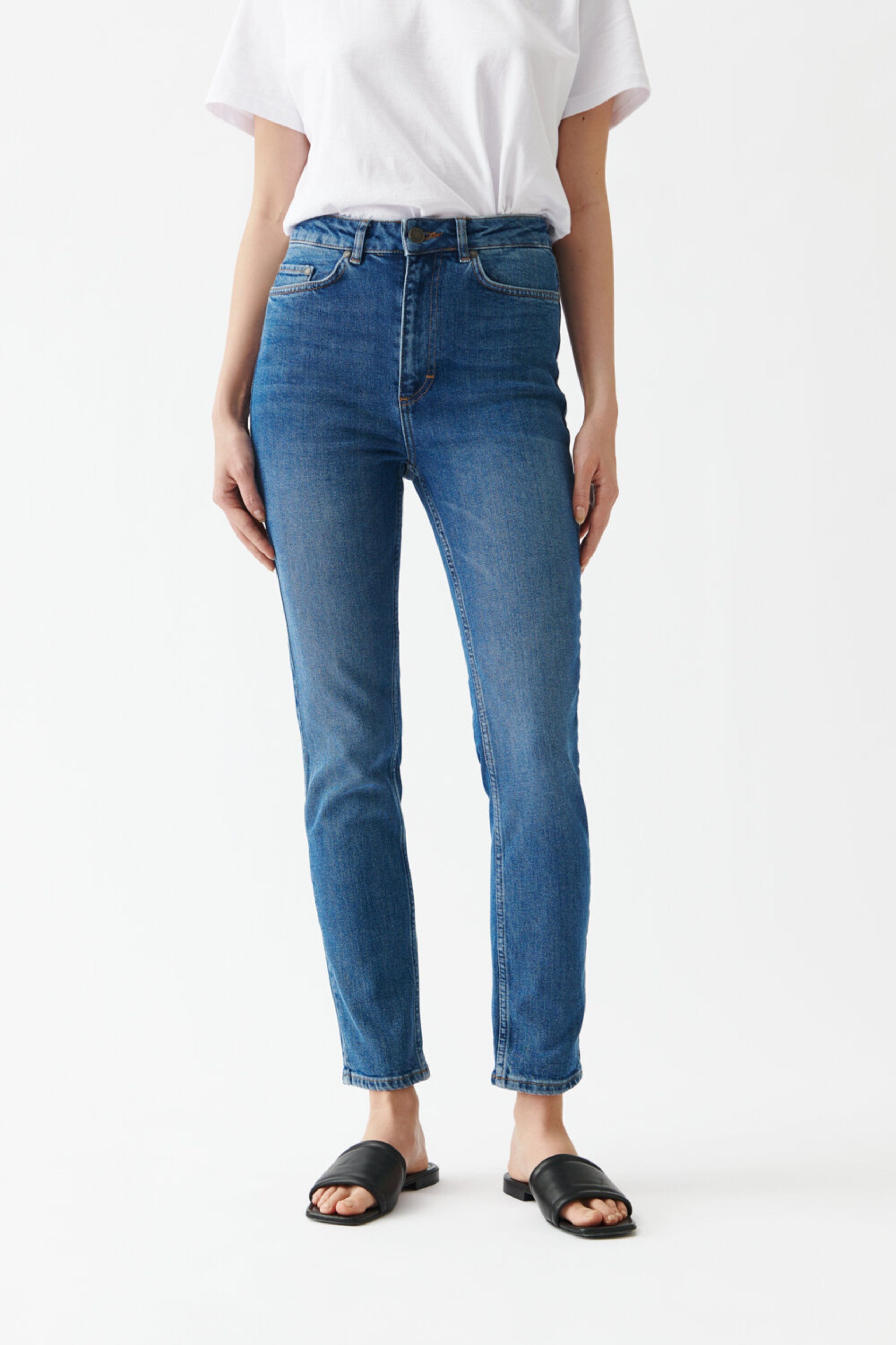 A woman wearing a white t-shirt and blue jeans, with Twist & Tango's Julie High Waist Skinny Jeans in Mid Blue.
