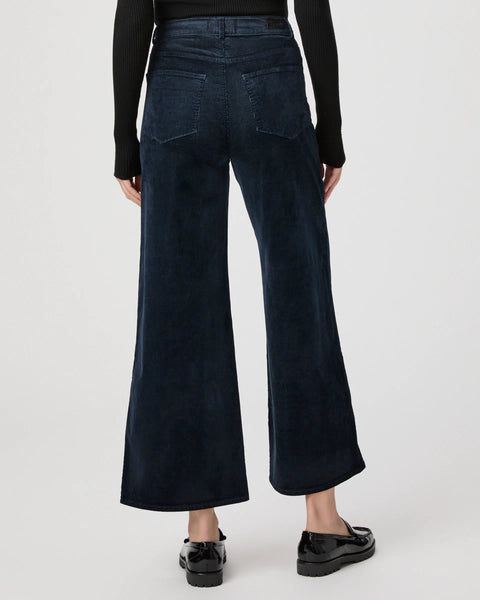 A person wearing navy high-rise Harper Ankle Wide Leg jeans by Paige and black shoes, photographed from the back against a plain background.