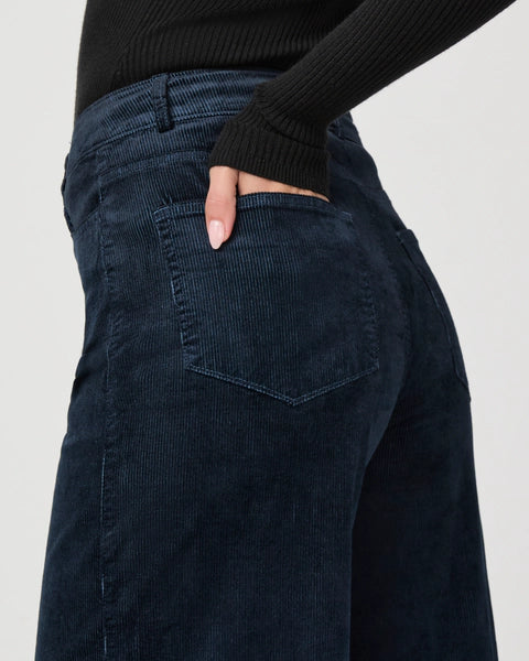 Close-up of a person wearing Harper Ankle Wide Leg in navy corduroy by Paige and a black knit long-sleeve top with a hand in the back pocket.