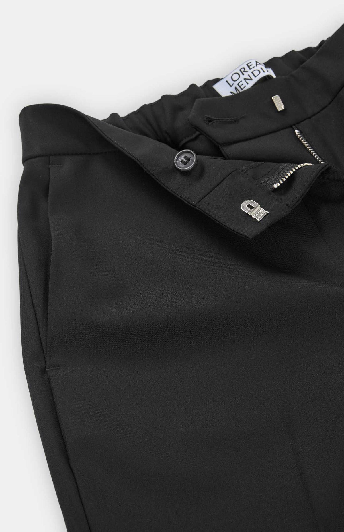 Close-up of the waistband and fly of the black Alaiak Trouser, featuring a button closure, zippered fly, and elasticized back.