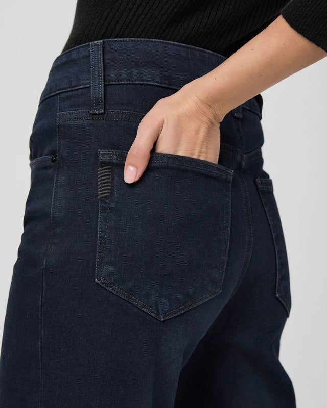 A person wearing Paige’s Sasha Wide Leg - Duchess dark wash jeans and a black top places their right hand in the back pocket of the jeans.