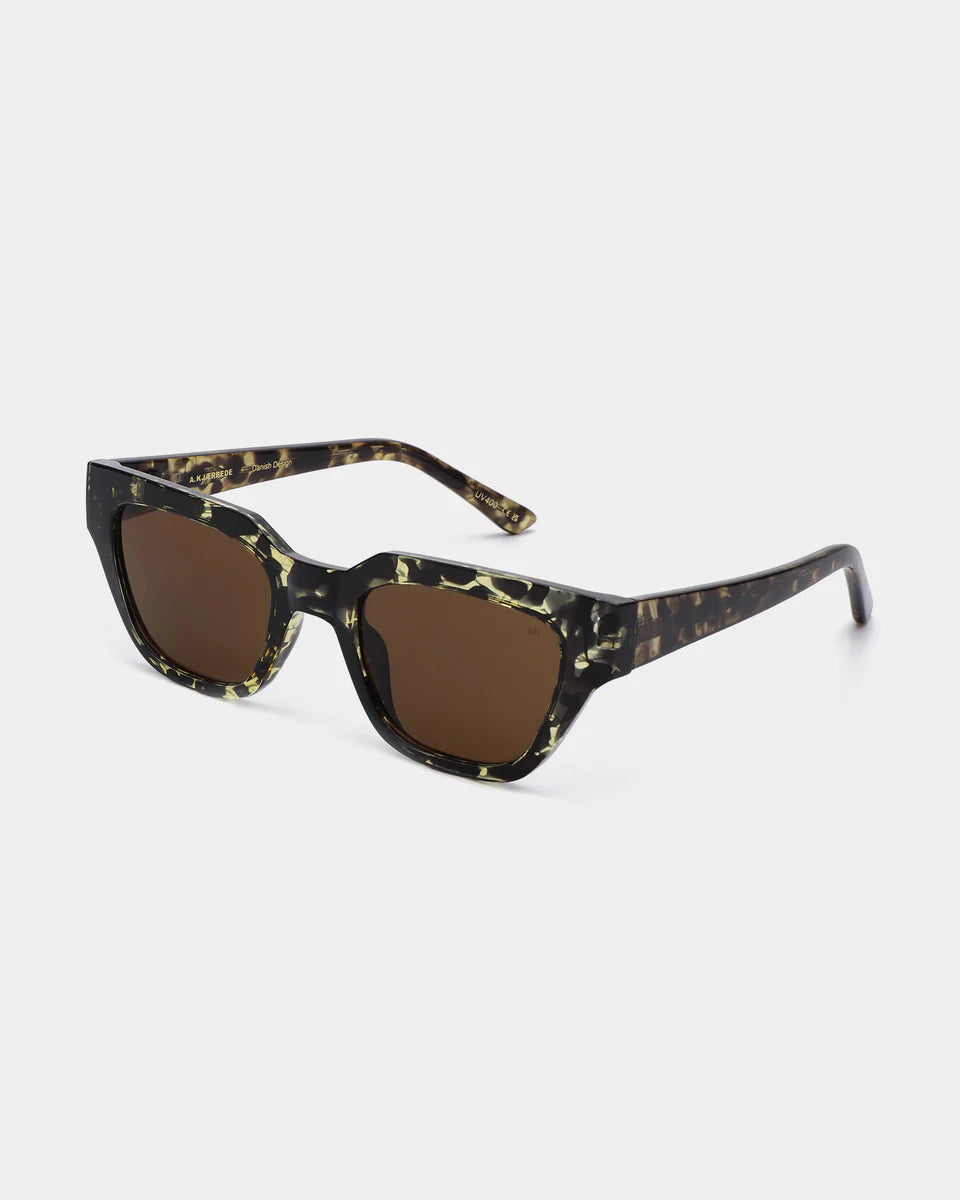 A. Kjærbede Kaws Sunglasses in Black/Yellow Tortoise feature a rectangular frame and brown lenses with UV 400 protection, shown on a plain white background.
