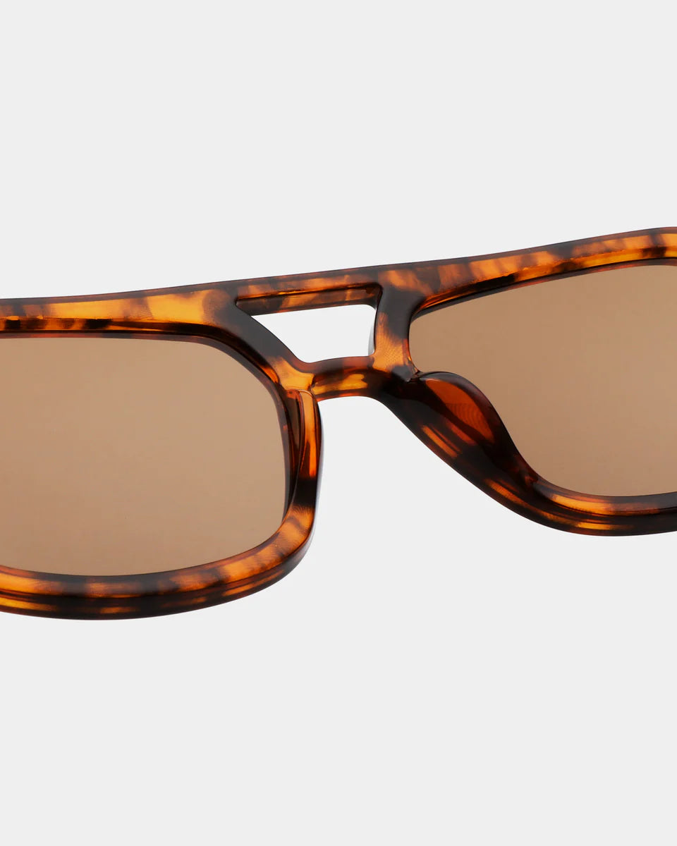 Close-up of A. Kjærbede Kaya Sunglasses - Havana, featuring an oversized pilot frame in brown tortoiseshell, double bridge, and UV 400 protected brown tinted lenses against a plain background.