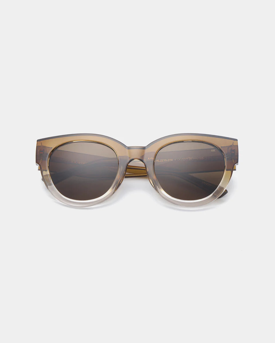 Lilly Sunglasses - Smoke Champagne by A. Kjærbede feature round frames in a translucent brown and beige gradient, crafted from recycled material with dark lenses, shown on a plain white background.