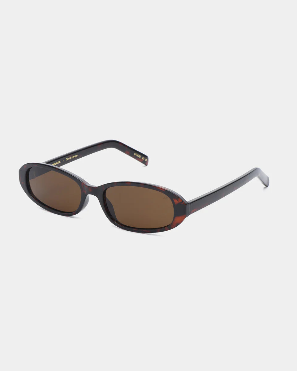 The Macy Sunglasses - Demi Tortoise by A. Kjærbede, featuring oval tortoiseshell frames and brown UV 400 lenses, are displayed at an angle on a plain white background.