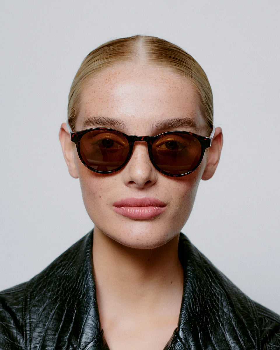 Person with slicked-back blond hair wears A. Kjærbede Marvin Sunglasses in Demi Tortoise and a textured black jacket, facing the camera against a plain background.