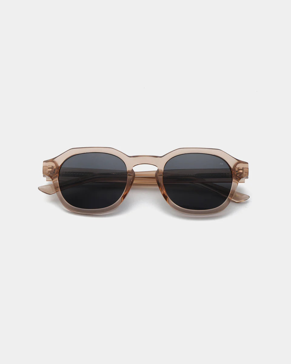 The Zan Sunglasses - Champagne by A. Kjærbede feature eco-friendly rectangular black lenses, translucent brown frames, and UV 400 protection, shown against a plain white background.