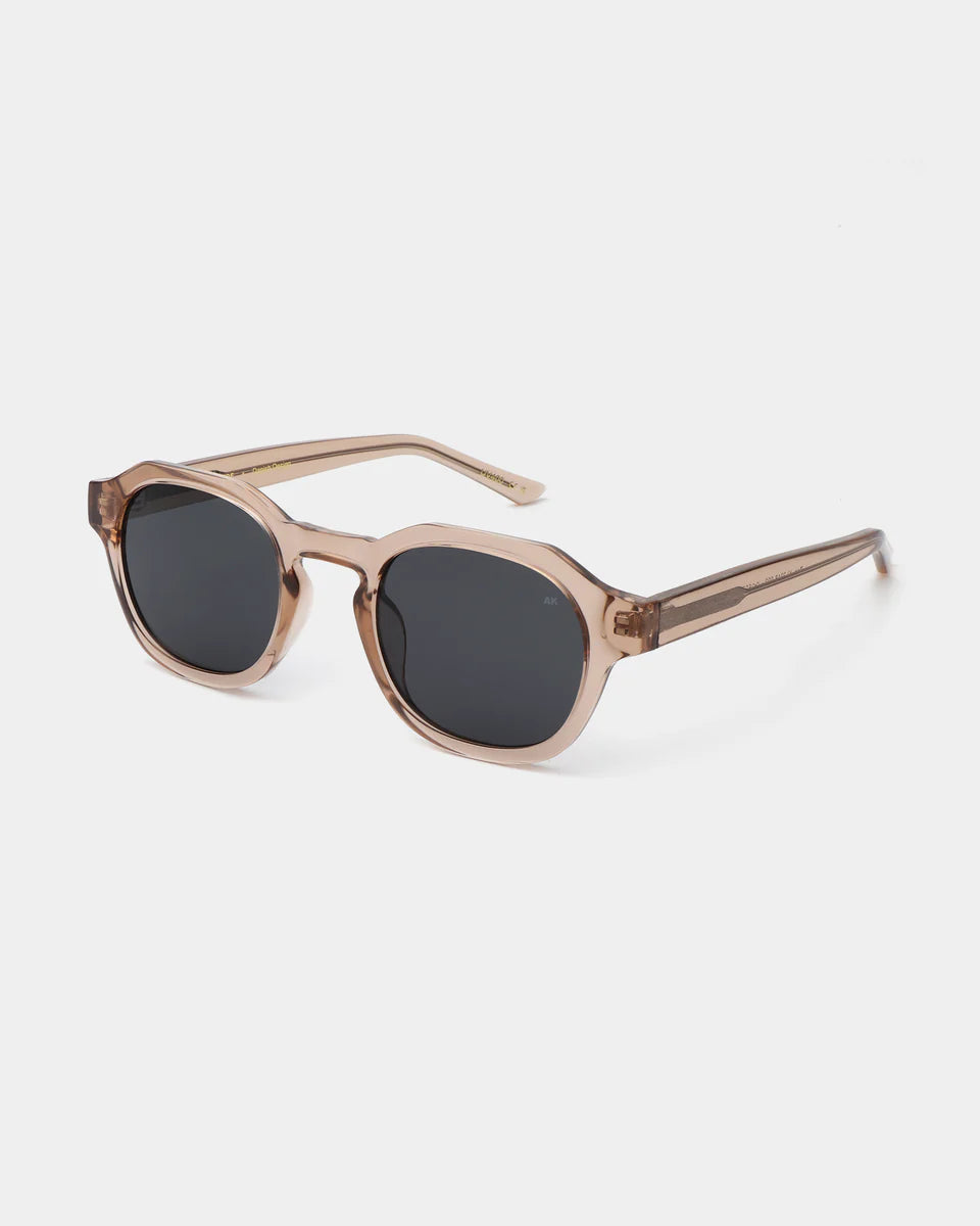 The Zan Sunglasses - Champagne by A. Kjærbede feature a brown translucent rectangular frame with black lenses, UV 400 protection, and are made from recycled materials. Displayed on a white background.