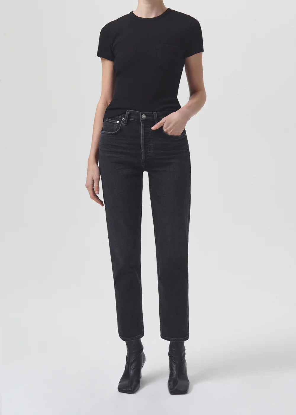 A woman wearing high-rise black jeans and a slim straight leg black t-shirt, the Riley Straight Crop - Panoramic by AGOLDE.