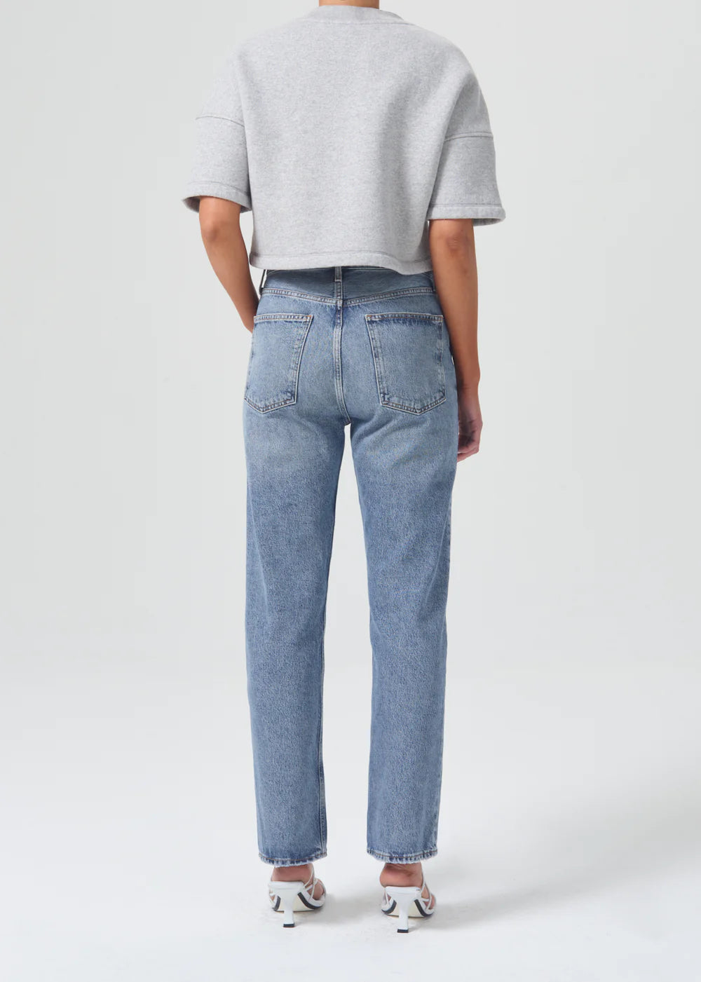 The back view of a woman wearing AGOLDE 90's Pinch Waist - Navigate jeans with a high-rise waist and an organic cotton grey sweater.