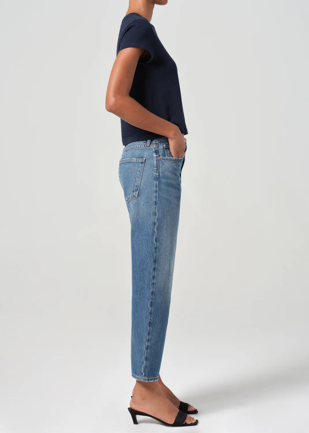 A person in a navy t-shirt and AGOLDE's 90's Straight Crop - Essence jeans paired with black heeled sandals stands in profile against a plain background.