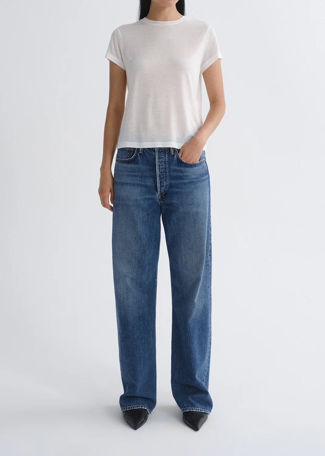 A person wearing a white short-sleeve t-shirt and AGOLDE Vintage Loose - Curb straight leg jeans in an indigo wash, standing against a plain light background with one hand in their pocket.