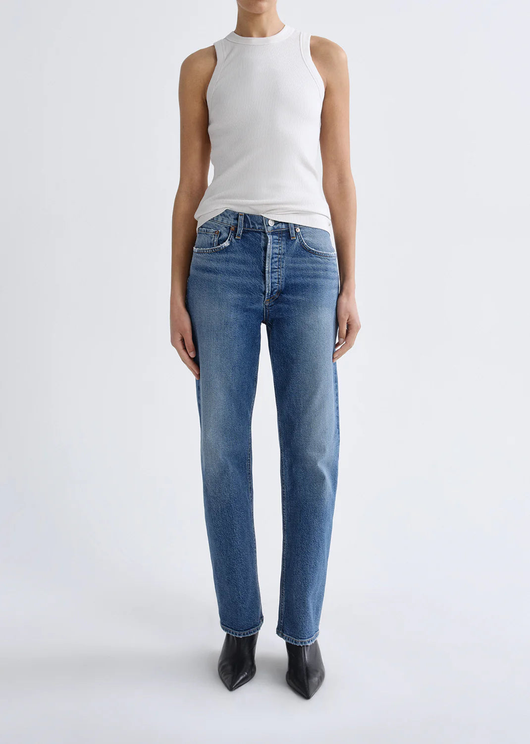 A person is wearing a white sleeveless ribbed top, AGOLDE Lana Jean - Waive (Comfort Stretch) in vintage indigo, and black pointed-toe shoes, standing against a plain white background.