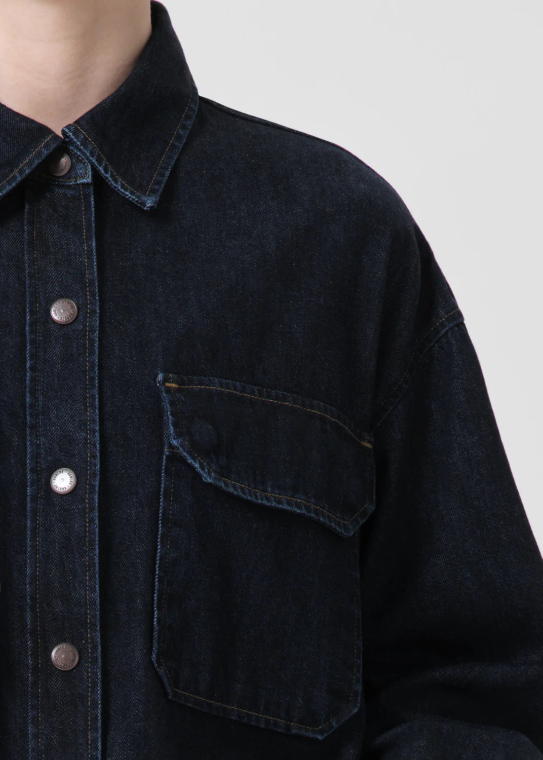 Close-up of a person wearing the AGOLDE Gwen Slice Shirt - Rinse, showcasing a black denim button-down design made from organic cotton, complete with a buttoned flap pocket on the left side.