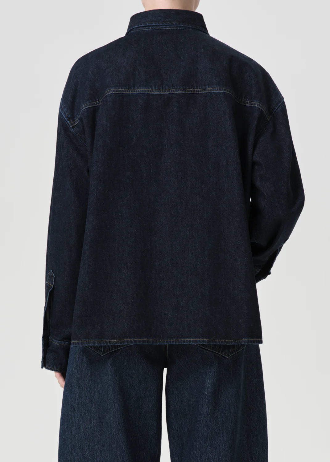 A back view of a person wearing the Gwen Slice Shirt - Rinse by AGOLDE, crafted from dark organic denim, along with matching pants, against a plain background.