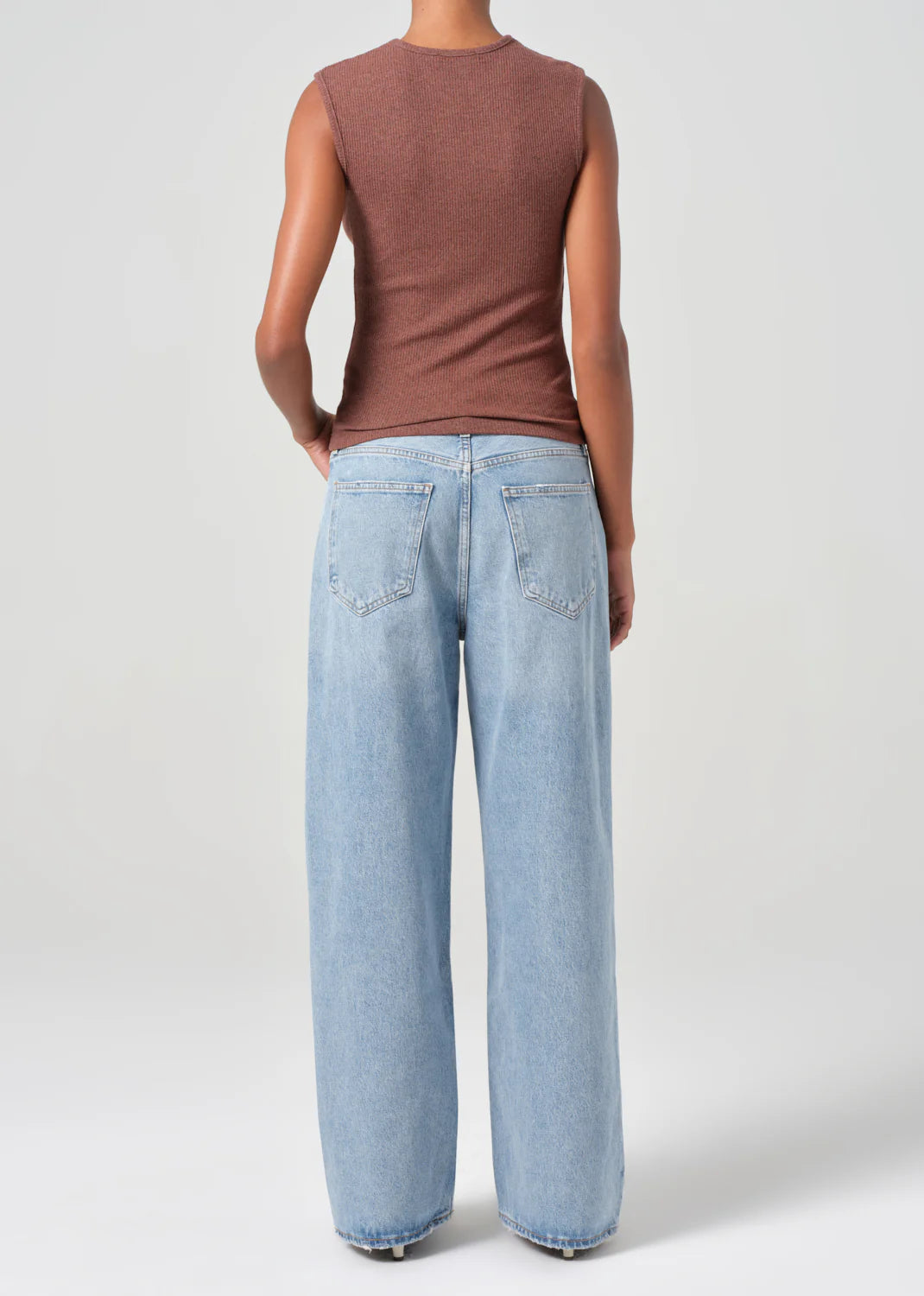 A person wears an oversize fit sleeveless brown top and AGOLDE's Low Slung Baggy 30.5" jeans in Force—light blue, crafted from organic cotton—set against a plain background.
.