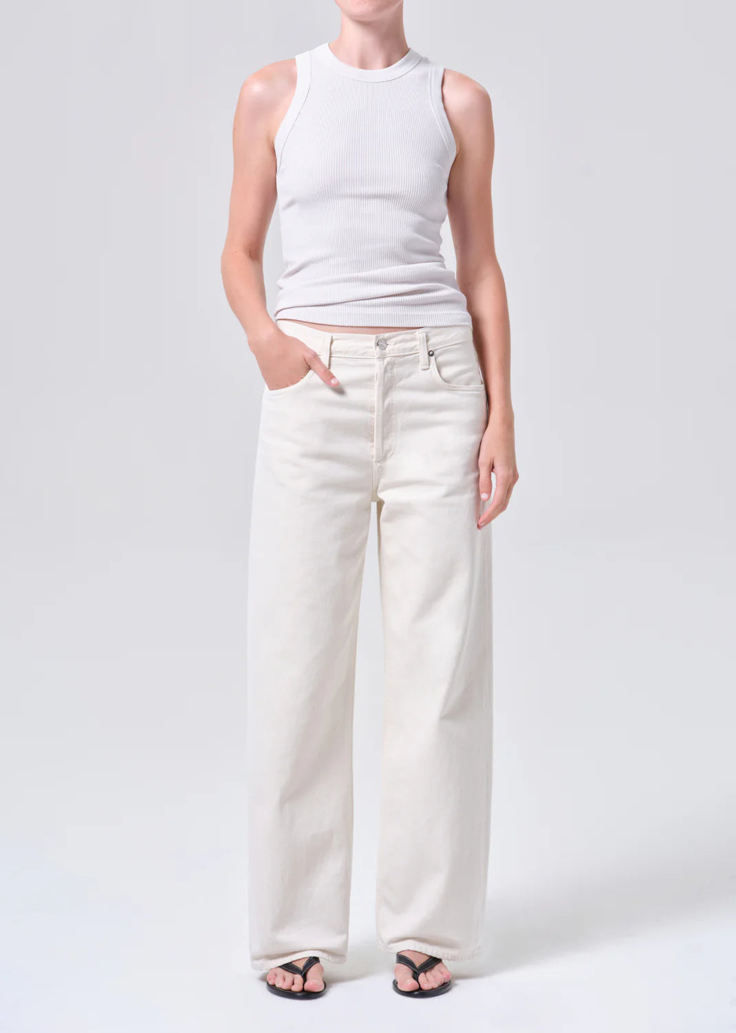 Person wearing a white sleeveless top and wide-leg white jeans on a light gray background