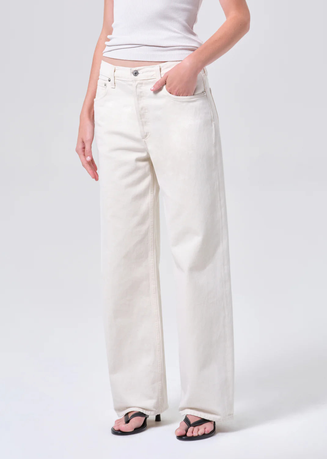 Person wearing a white sleeveless top and wide-leg white jeans on a light gray background