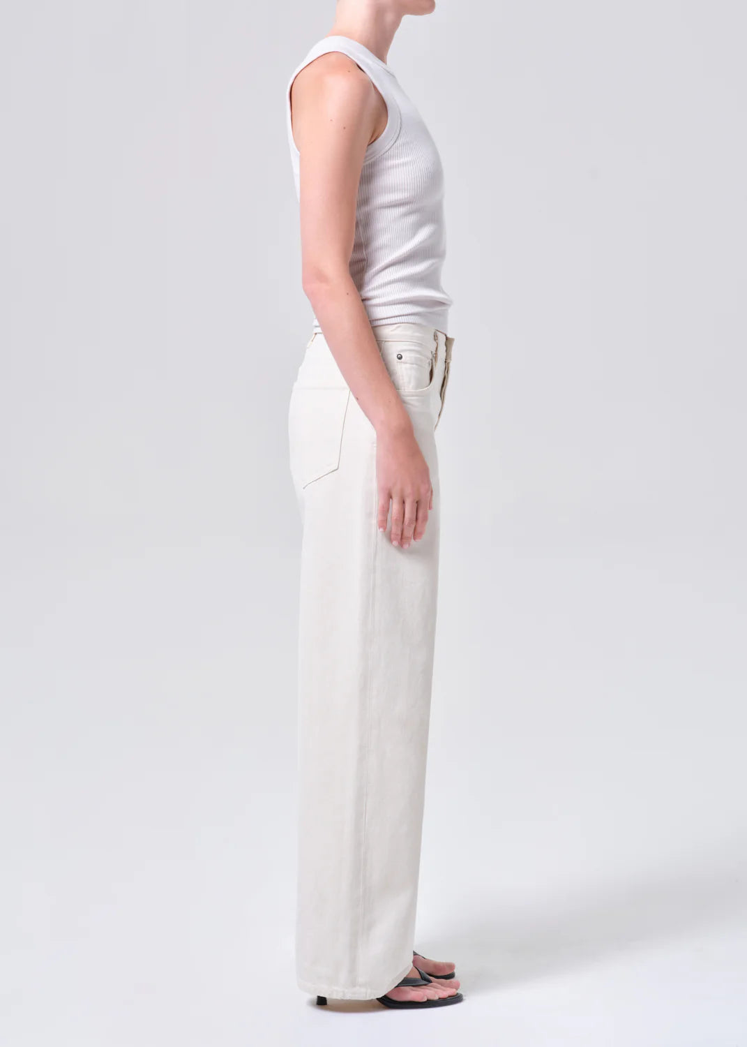 Person wearing a white sleeveless top and wide-leg white jeans on a light gray background