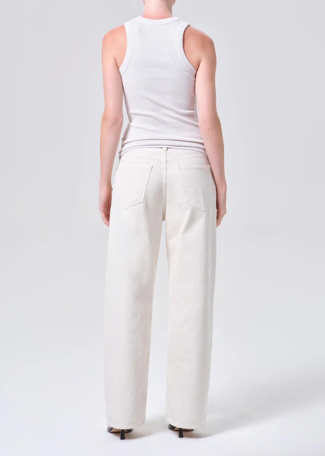 Person wearing a white sleeveless top and wide-leg white jeans on a light gray background