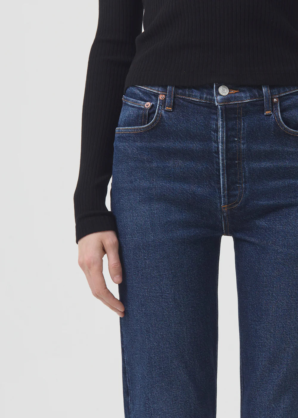 The back view of a woman wearing AGOLDE Riley Straight Long - Divided jeans with a high-rise and slim straight leg, paired with a black turtleneck.
