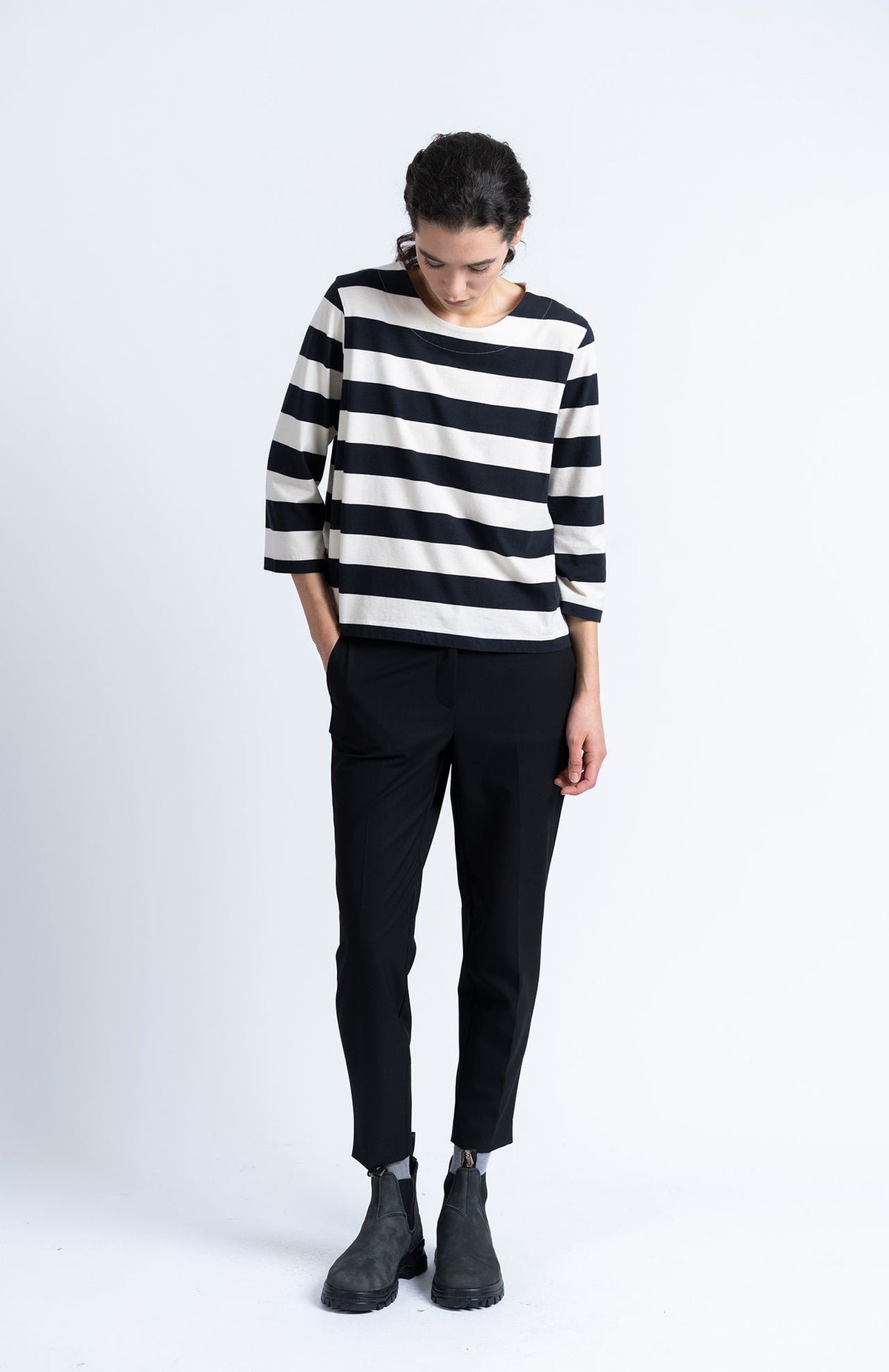 A person wearing a black and white striped three-quarter sleeve top, Alaiak Trouser - Black joggers, and dark ankle boots.