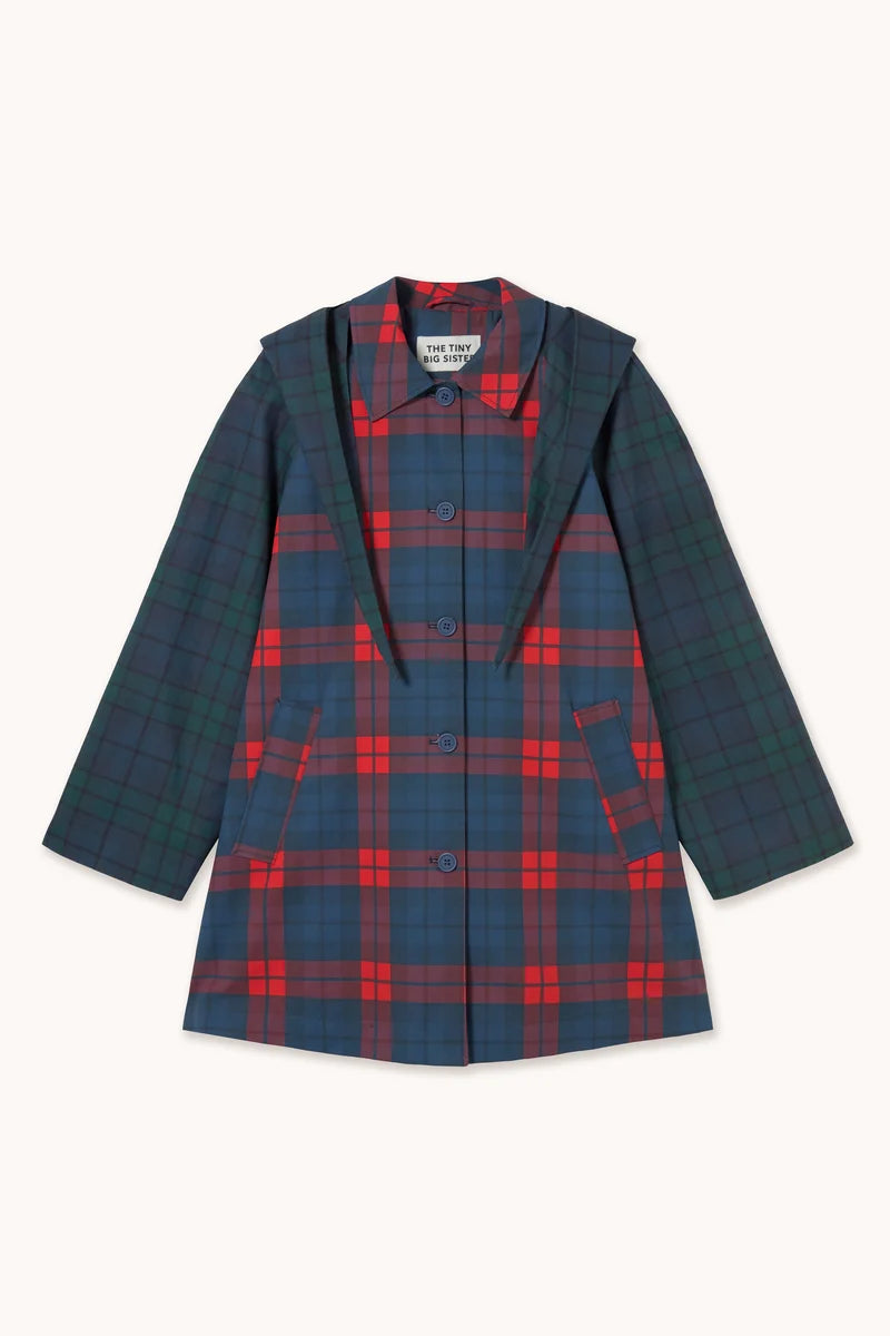 The Tiny Big Sister Check Hood Trench Coat is a children’s hooded trench coat featuring a blue, green, and red plaid pattern, front buttons, two slanted pockets, and crafted from water-resistant cotton for practical everyday wear.