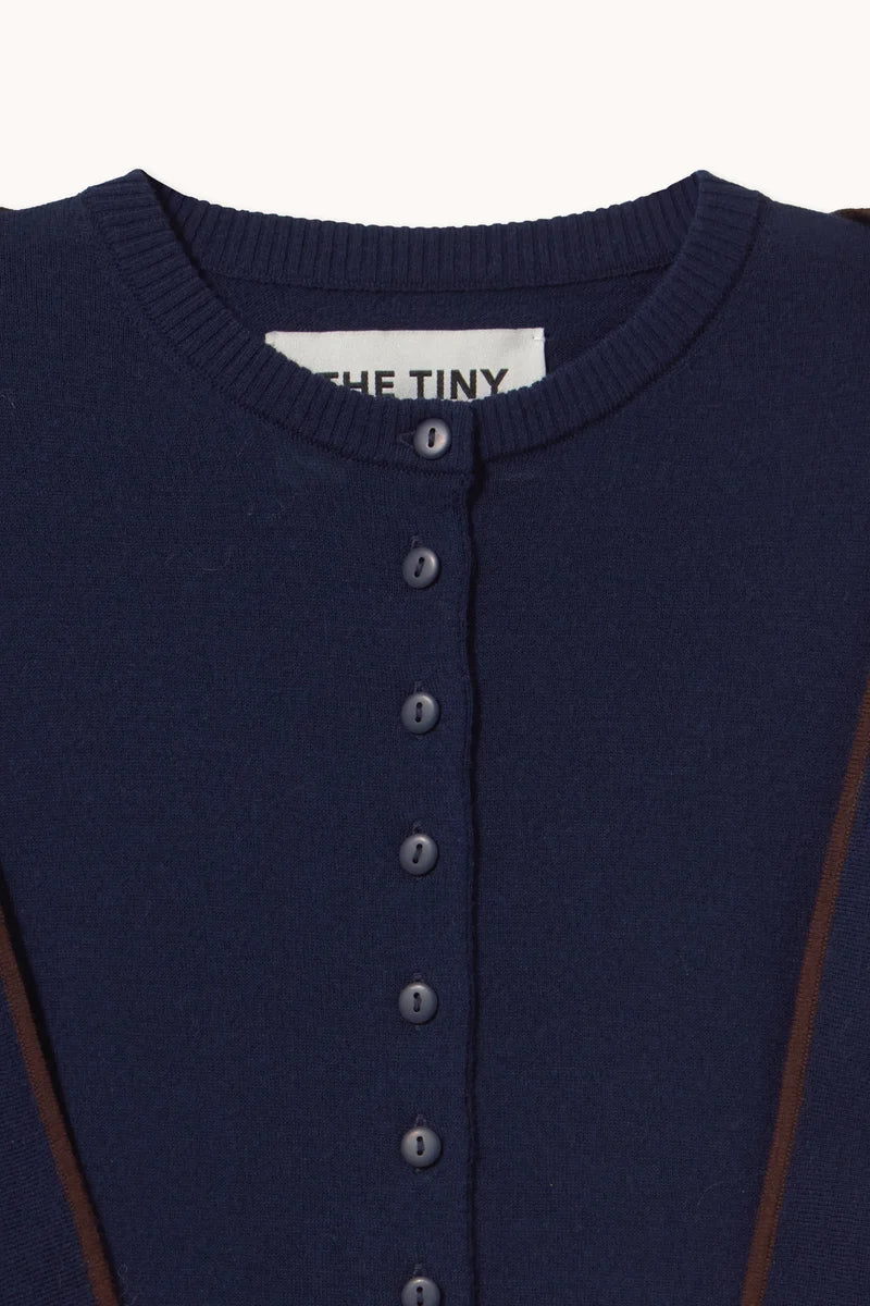 Close-up of a navy blue knit cardigan sweater with a button-up front and a visible neck label reading 'THE TINY'.