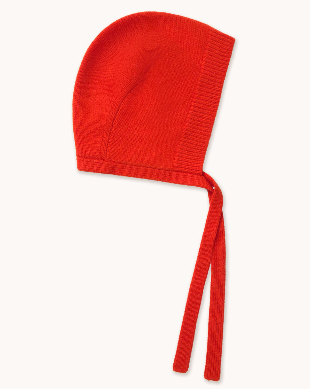 The Tiny Big Sister Merino Bonnet - Summer Red features a minimalist silhouette with a ribbed edge and two long straps, shown laid flat on a white background.