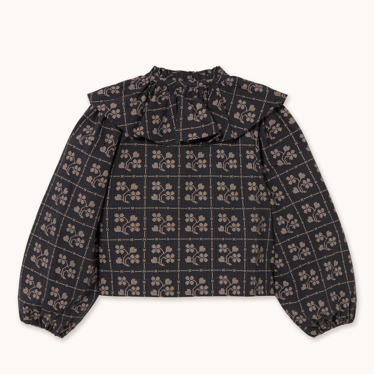 A long-sleeve blouse with a ruffled high collar, featuring a dark charcoal gray and black grid pattern overlaid with small beige floral motifs, laid flat against a light off-white background.