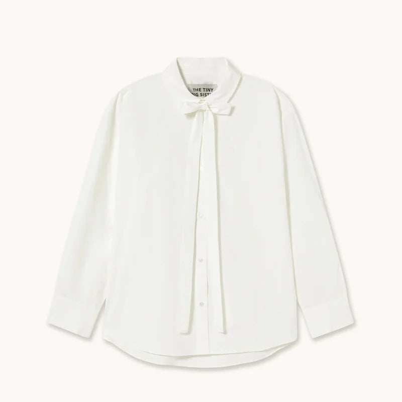 A white long-sleeve blouse with a pointed collar and a matching fabric bow at the neck, displayed flat against a solid off-white background.