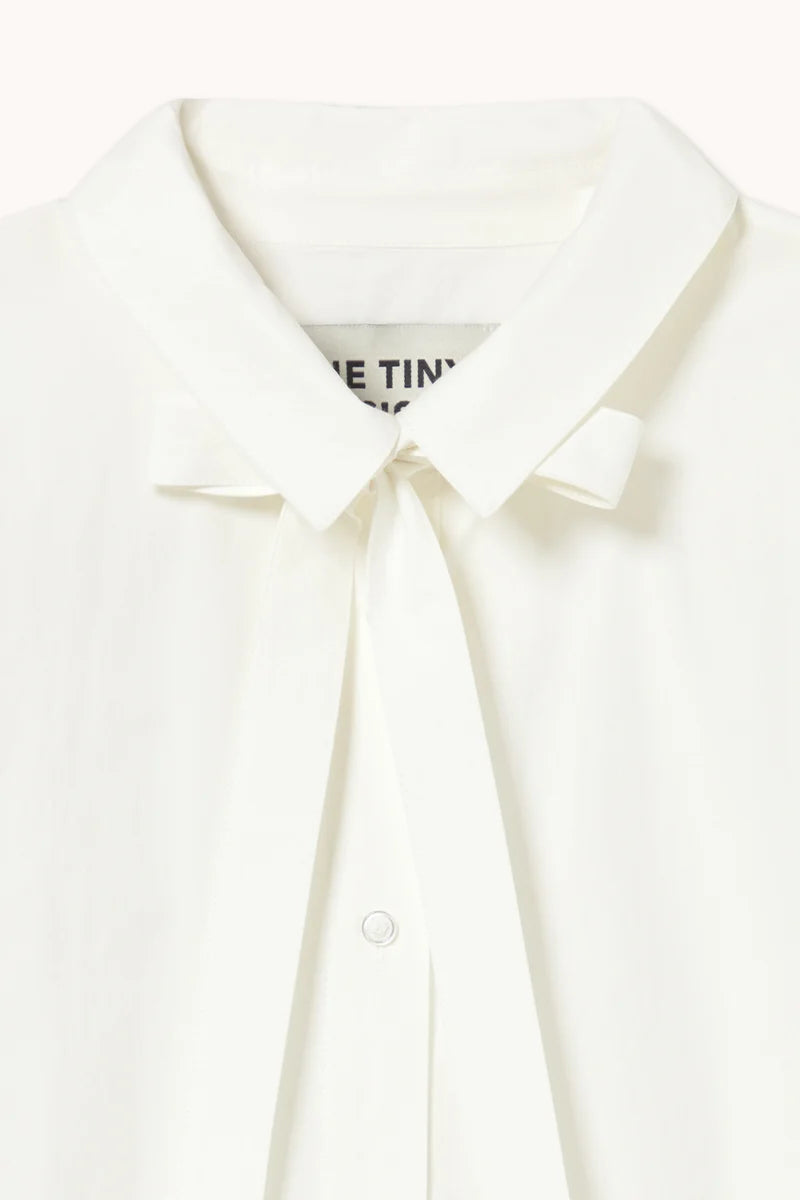 Close-up of the Bow Neck Shirt in Off White by Tiny Big Sister, a feminine blouse featuring a white collar and bow tie detail at the neckline, with a partially visible label inside the collar.