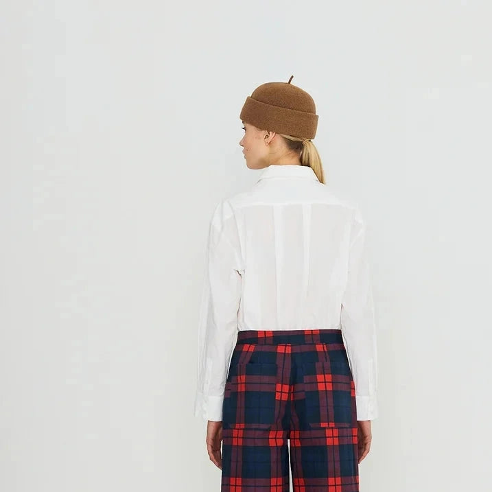 A model shown from the back wearing a white long-sleeve shirt, red and navy plaid wide-leg trousers, a brown beret, and red shoes, set against a plain white studio background.