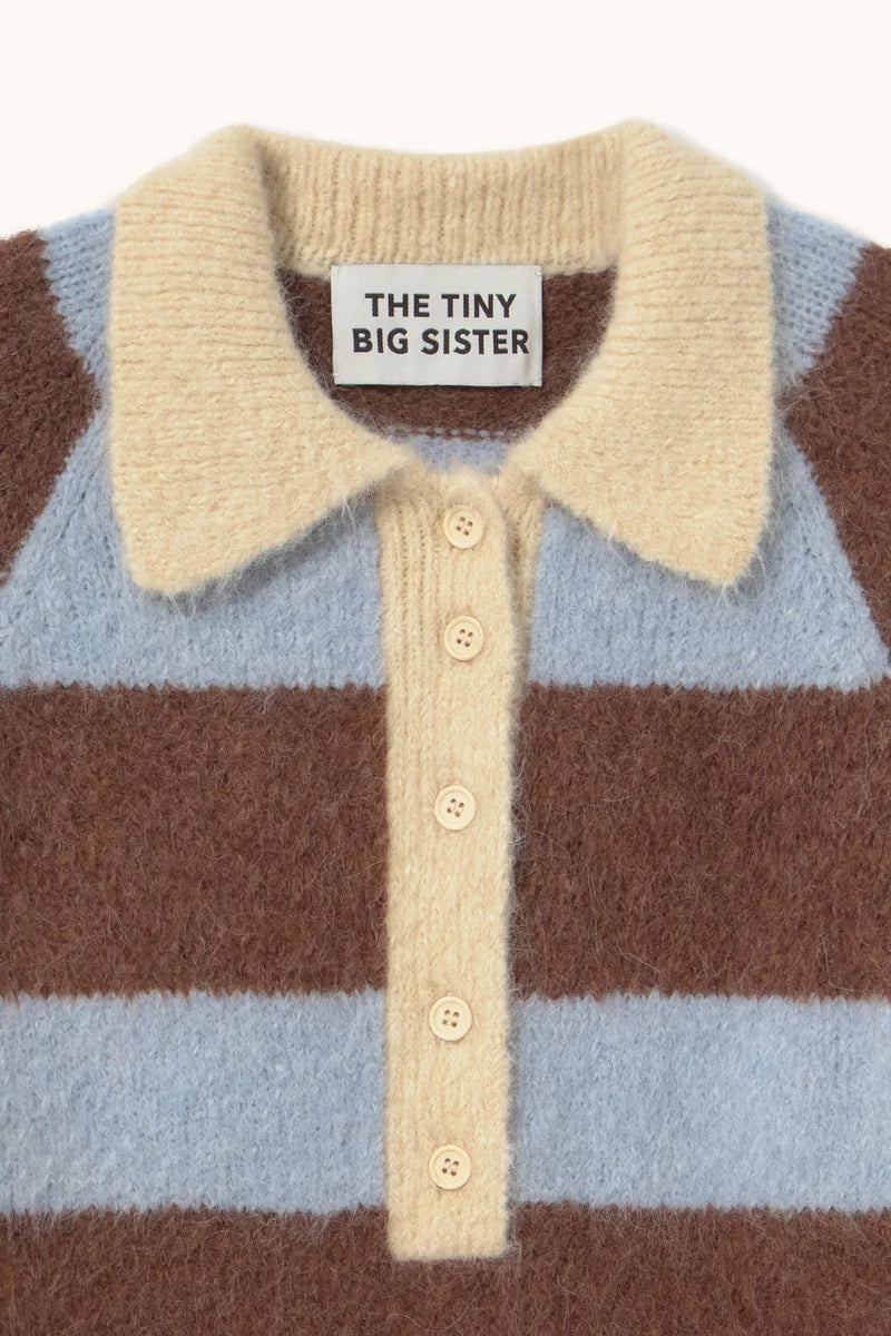 Close-up of a fuzzy knit polo shirt with horizontal brown and light blue stripes, a cream collar, and a cream button placket. The neck label reads 'THE TINY BIG SISTER'.