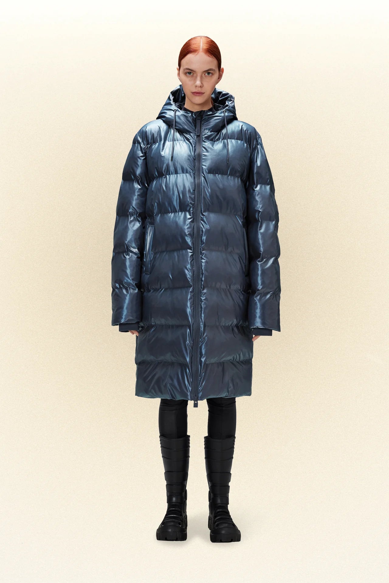 A woman is standing in a Rains Alta Long Puffer Jacket.