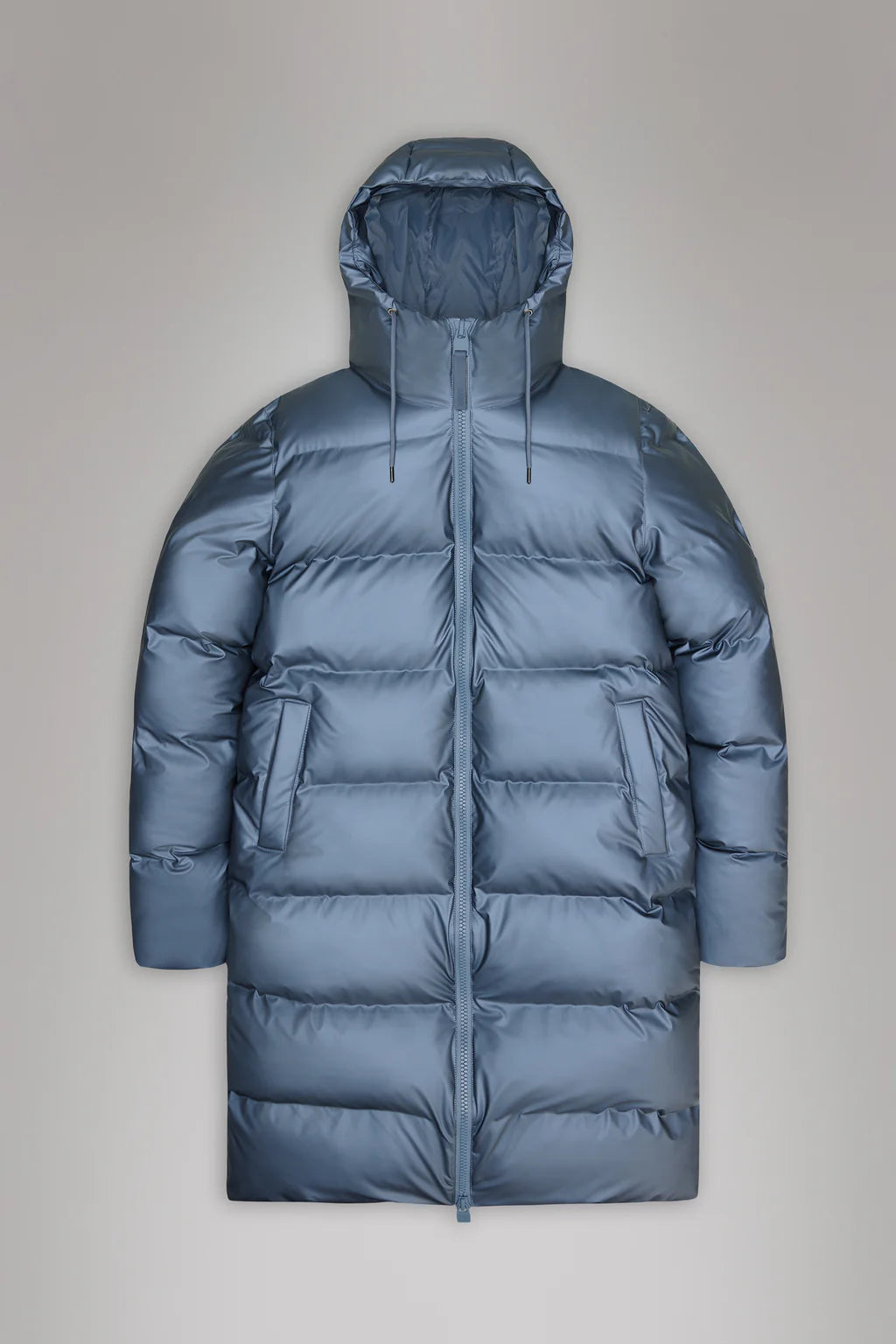 The Alta Long Puffer Jacket by Rains is a grey winter coat featuring a hood, two large front pockets, breathable fabric, and featherless chamber technology.