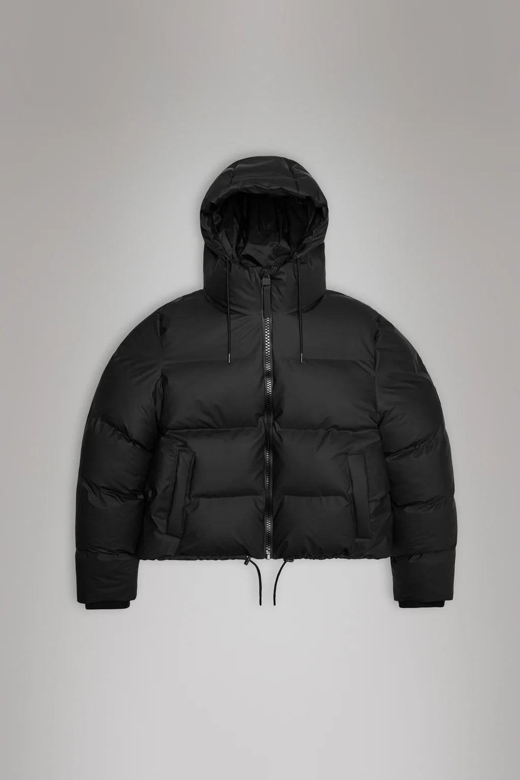 The Alta Short Puffer Jacket by Rains is a black, waterproof, puffer-style hooded winter jacket featuring a front zip, two large pockets, and drawstrings at the hem.