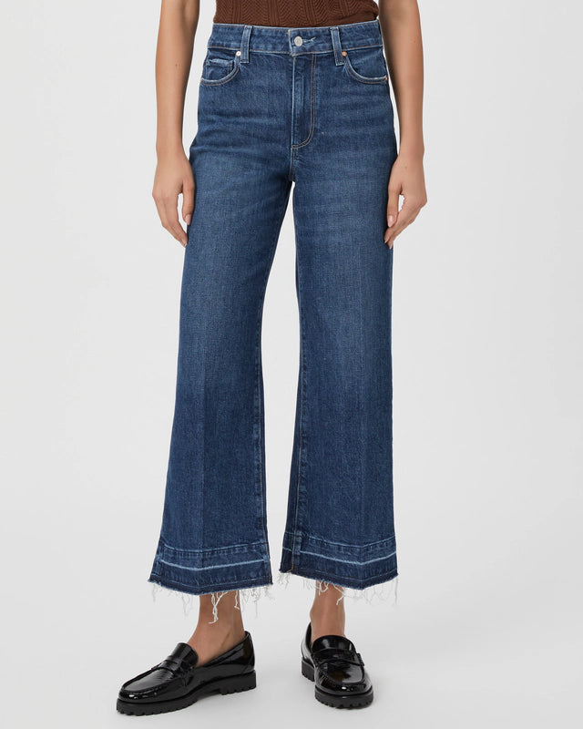 Person wearing the Paige Anessa Wide Leg - Alana ultra high-waisted blue jeans with frayed hems and black loafers, standing against a plain white background.